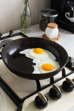 Two eggs are fried in a cast iron skillet in the home kitchen .. Concept for preparing homemade food. Homemade food is always prepared with love and has a special taste.の写真素材