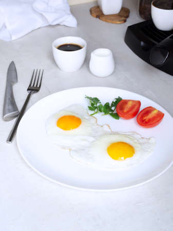 Two fried eggs with tomatoes and herbs on a white plate. Flexitarian concept. Some diets and food principles include an egg breakfast. Vertical orientation.の写真素材