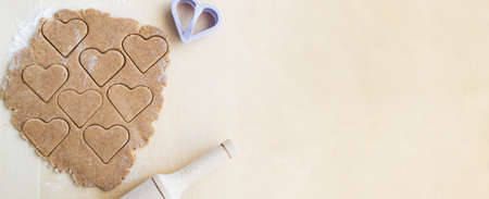 The process of making heart-shaped whole wheat flour cookies with a rolling pin and a cookie cutter. The concept of festive home baking for loved ones. Valentine's Day. top view. Banner. copyspace.の写真素材