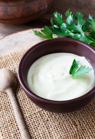 Homemade mayonnaise in a brown bowl with a sprig of green parsley on a wooden table. The concept of proper nutrition. rustic. vertical orientation.の写真素材