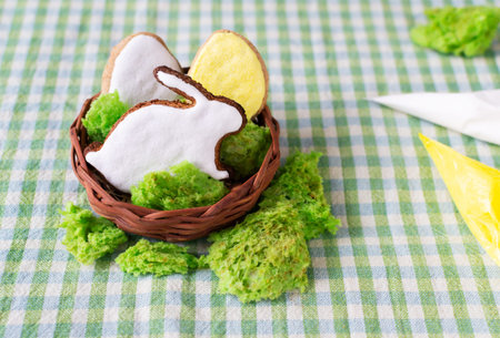 Easter gingerbread in the shape of eggs and hares with colored icing in a wicker bowl with green...