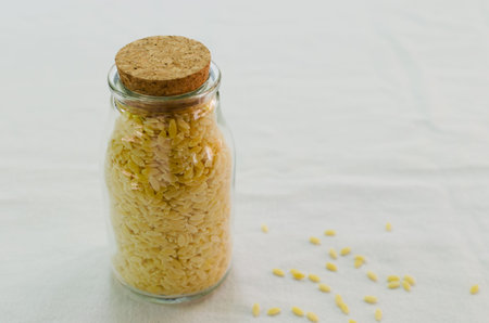 Raw Italian risoni pasta in a glass jar on a table. The concept of traditional cuisine. vertical...
