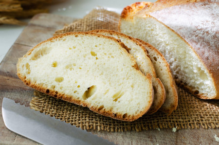 Slices of fresh baked bread on burlap with a knife on a light background. rustic style. The concept...