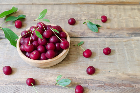 Many ripe red cherries in a wooden bowl on a wooden table. Healthy food concept. horizontal...