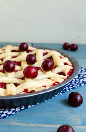 Homemade cherry pie in a round shape on a blue wooden table. The concept of traditional baking. Seasonal pie. vertical orientation.の写真素材