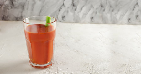 One transparent glass cup with red tomato juice and a sprig of celery on a light background. Healthy...