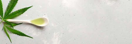 Cannabis CBD hemp oil in a white teaspoon with green leaves on a gray background. The concept of Alternative Oil. horizontal orientation. Banner. copy spaceの写真素材