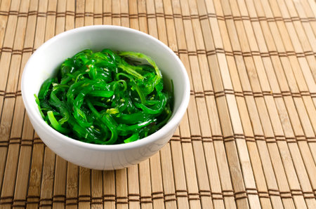 Hiyashi Wakame Chuka or seaweed salad in a white bowl on a wooden background. The concept of traditional oriental food.の写真素材