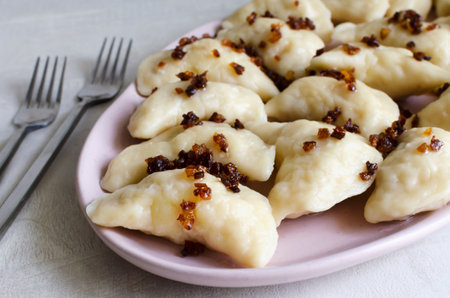 Boiled Vareniks stuffed with potatoes and fried onions on a pink plate. The concept is traditional Ukrainian cuisine. horizontal orientation.の写真素材