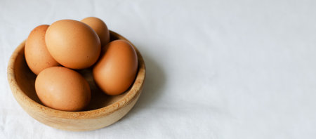 Several chicken eggs in a wooden bowl on a white tablecloth. rustic style. The concept of organic food. horizontal orientation. Banner. copyspace.の写真素材