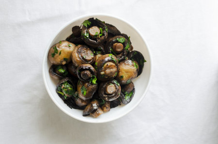 Fried champignons with garlic and parsley in a white bowl on the table. The concept of vegetarian food. horizontal orientation. selective focus. top view.の写真素材