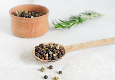 A mix of black, white, red and allspice peppercorns in a wooden spoon on a light background. spice dried peppercorn concept. horizontal orientation. selective focus.の写真素材