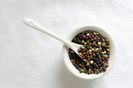A mix of black, white, red and fragrant peppercorns in a white bowl on a light background. spice dried peppercorn concept. vertical orientation. selective focus. copyspace. top view.の写真素材