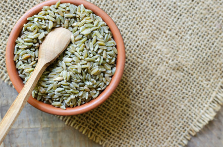 Raw freekeh or firik in ceramic bowl with spoon on burlap on wooden background. Concept of healthy food. Vegan and vegetarian food. horizontal orientation. top view. copyspace.の写真素材
