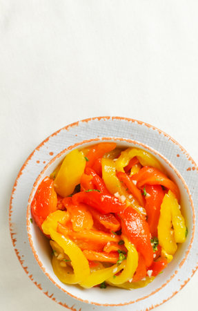 Sliced red and yellow roasted peppers in a white ceramic bowl. Concept of healthy eating. Traditional Italian dish. Vegetarian and vegan food. vertical orientation. top view. copy spaceの写真素材