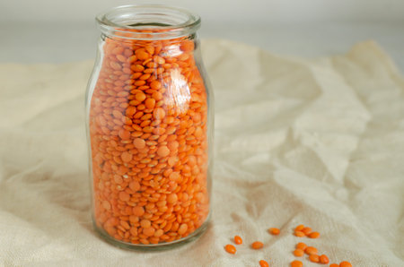 Orange lentils in a glass jar on a linen tablecloth. The concept of proper nutrition. Vegan and vegetarian food. Horizontal orientation. Copy spaceの写真素材
