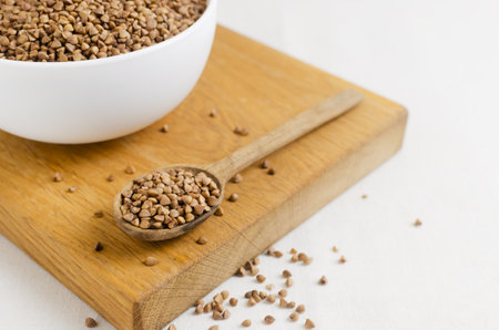 Organic dry buckwheat groats in a white bowl with a wooden spoon on a wooden cutting board. Rural style. Vegetarian and vegan food. Concept of healthy eating. Horizontal orientation. Selective focusの写真素材