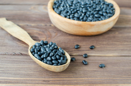 Raw black bens in wooden spoon and bowl on wooden table. Rural style. Vegetarian food concept. Horizontal orientation. Selective focus.の写真素材