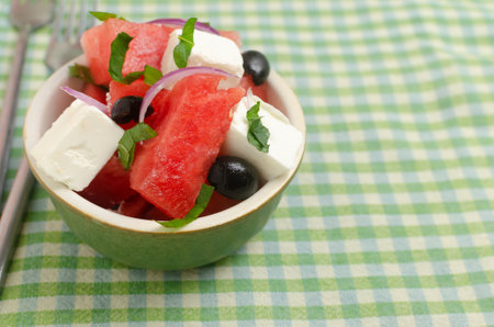 Summer salad with watermelon, feta cheese, olives and mint in a green bowl on a green napkin. Concept of healthy eating. Vegan, vegetarian. Horizontal orientation. Copy spaceの写真素材