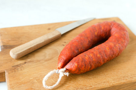 Spanish Chorizo sausage with red pepper, paprika and garlic on a wooden cutting board with a knife. Traditional Mediterranean food concept. Horizontal orientation. Selective focus.の写真素材