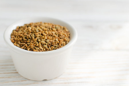 Dry fenugreek or shambhala in a bowl on a white wooden table. Medicinal plant from the Middle East. Alternative medicine concept. Selective focus. Copy space. Horizontal orientationの写真素材