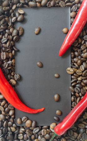 Bar of extra dark chocolate with three red chili peppers on a background of coffee beans. Trend food concept. Selective focus. Vertical orientation. Top viewの写真素材
