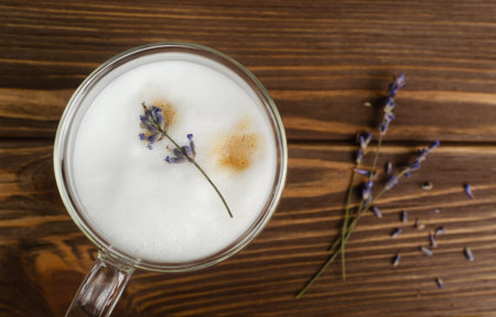 Large glass of hot Lavender Latte on a brown wooden table with flowers in the background. Concept of high-quality coffee drinks. Horizontal orientation. Selective focus. Copy space. Top viewの写真素材