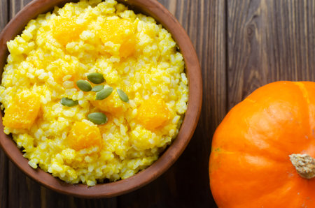 Pumpkin risotto in a ceramic bowl on a brown wooden table. Italian food concept. Rustic style. Autumn food. Selective focus. Horizontal orientation. Top viewの写真素材