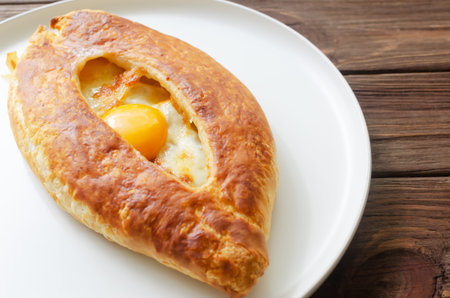 Adjarian khachapuri with egg yolk on a gray plate on a wooden table in the kitchen. The concept of...