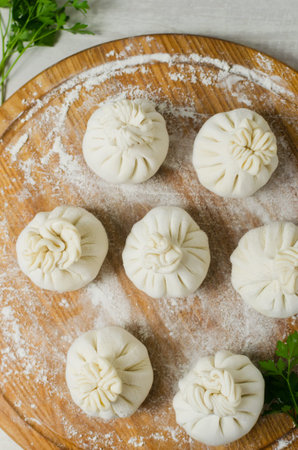 Raw khinkali with parsley on a round cutting board with flour on the table. Concept of traditional...