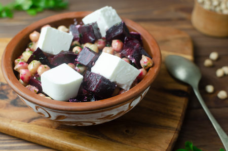Beet Salad with chickpeas, feta and green sauce with butter and parsley in a ceramic bowl on a wooden table. Rustic style. Healthy eating. Horizontal orientation. Selective focus.の写真素材