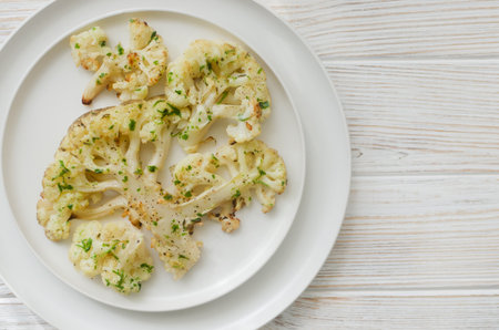 Cauliflower with chimichurri sauce on a white plate on a white wooden background. Concept of vegan and vegetarian food. Healthy eating. Horizontal orientation. Selective focus. Top view. Copy spaceの写真素材