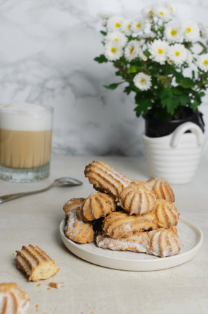 Tasty shortbread cookies with beautiful edges and powdered sugar next to a glass of cappuccino. Coffee time concept. Selective focus. Vertical orientationの写真素材