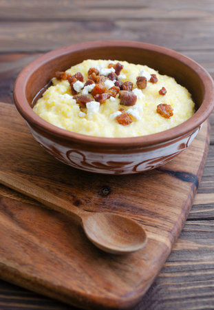 Classic banosh with bryndza and bacon slices in a decorative ceramic bowl on a wooden table. Traditional Ukrainian dish made from corn flour. Traditional cuisine concept. Selective focus. Copy spaceの写真素材