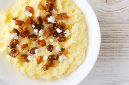 Traditional Hutsul banosh with bryndza and crispy cracklings in a white bowl on a wooden table. Authentic Ukrainian cuisine dish with a warm homely feel. Selective focus. Top view. Copy spaceの写真素材