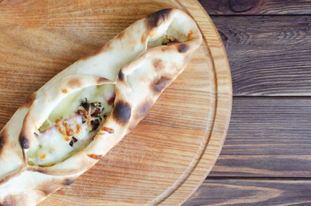 Modern street food pizza with mushrooms, sausage and melted cheese on cutting board on wooden table. Delicious fast food concept in lifestyle food photography. Top view. Copy spaceの写真素材