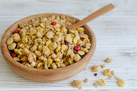 Rustic wooden bowl filled with crunchy granola, oats, cornflakes, puffed cereal clusters and dried...