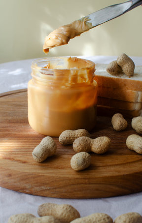 A fresh still life with a jar of creamy peanut butter, a knife with a generous portion of the...