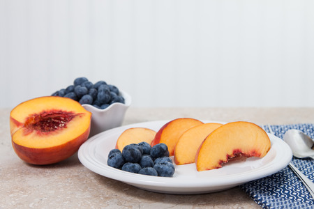 Sliced peaches and blueberries are served on a white plateの写真素材