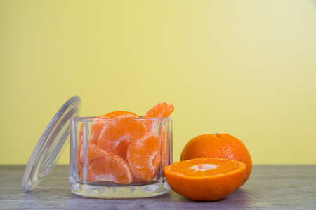 Mandarin orange slices in a glass jar sit on a wooden table with a bright yellow の写真素材
