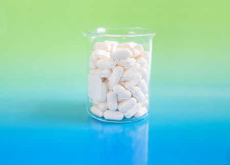 Beaker of white pills on a green and blue backgroundの写真素材