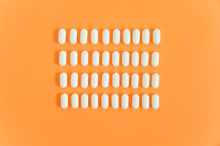Orderly rows of white pills on an orange background