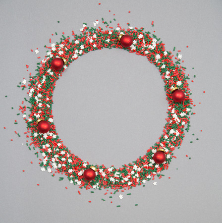 Christmas wreath made of red and green sprinkles with christmas ornaments on a grey backgroundの写真素材
