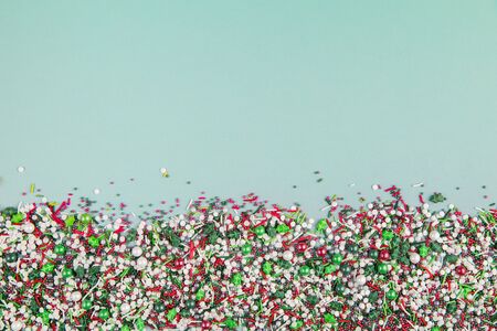 Flat lay of colorful christmas themed sprinkles along the bottom edge of a pastel green backgroundの写真素材