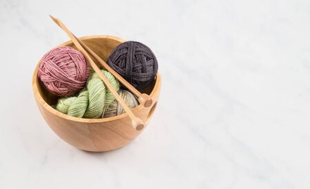 Knitting bowl full of balls of colorful yarn with wooden knitting needles on neutral backgroundの写真素材