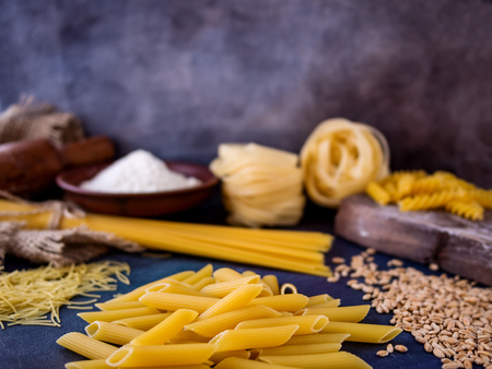 Italian pasta, spaghetti, fettuccine, penne, rolling pin, flour on a textured background. Still life in a rustic style.の写真素材