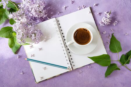 Romantic, business, breakfast. A sprig of lilac, a notebook, a cup of coffee, a pencil, lying on a purple textured background.top viewの写真素材