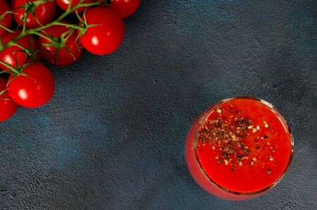 Glass cup with tomato juice with ground black pepper and cherry tomatoes on dark background. top viewの写真素材