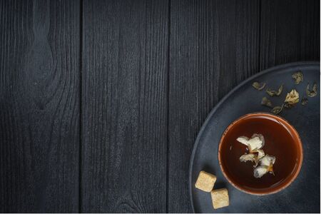 Green tea with jasmine in a clay cup on a black plate with pieces of cane sugar, on a black wooden background.の写真素材