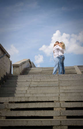 Young man holding his girlfriend by the waist against white clouds の写真素材